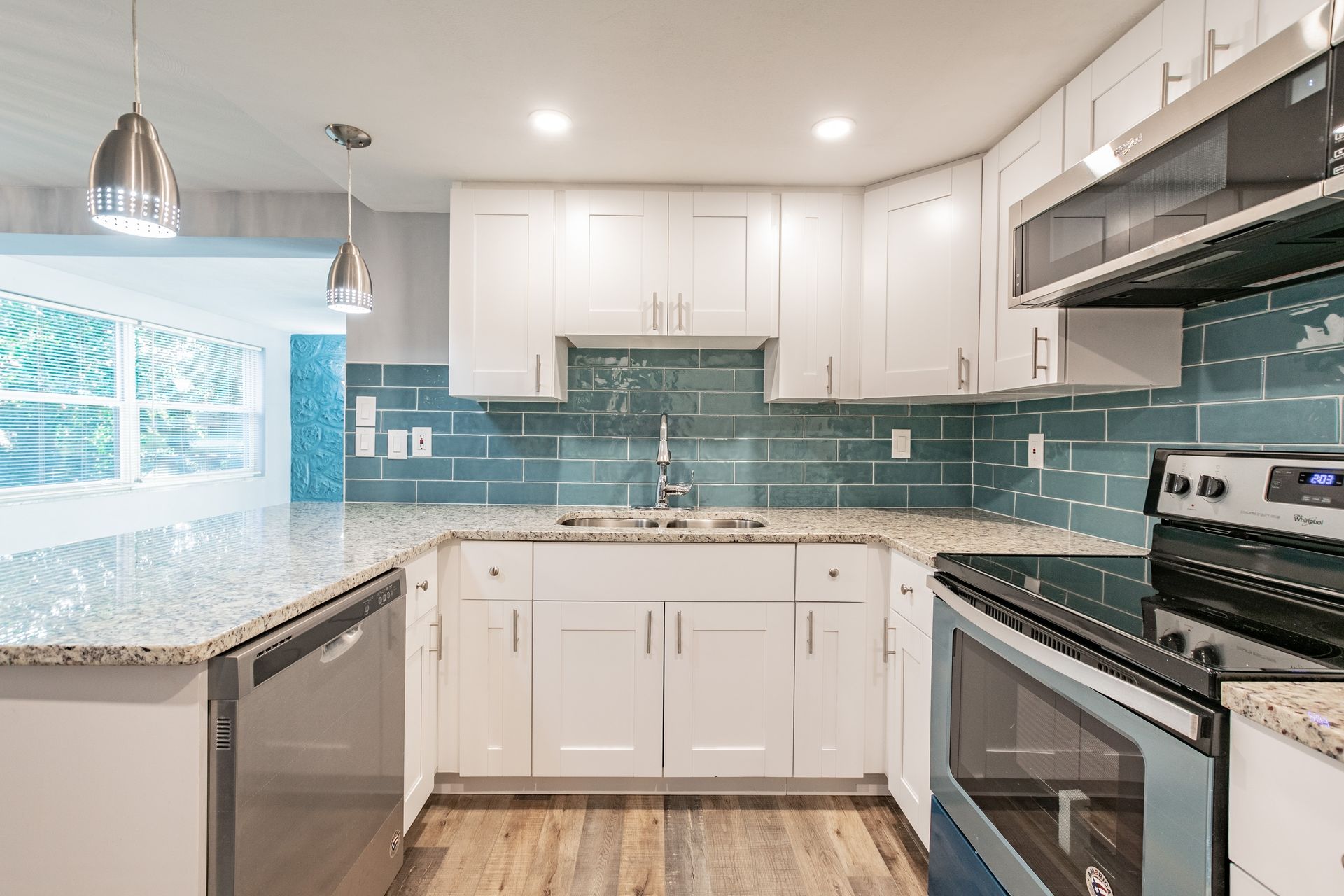 Modern kitchen with white cabinets, granite countertops, teal subway tile backsplash, and stainless steel appliances.
