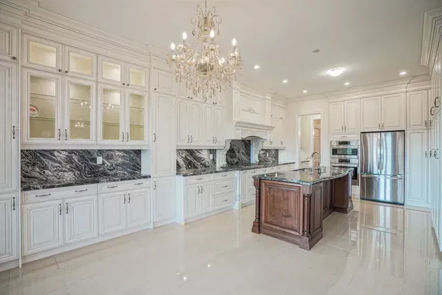 Elegant white kitchen with dark countertops, wood island, and chandelier.