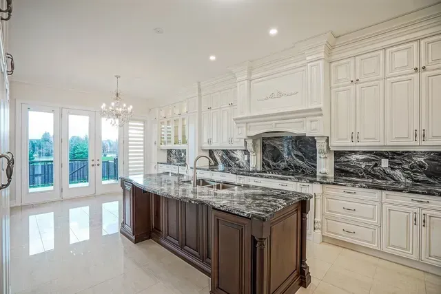 Elegant white kitchen with dark wood island and marble countertops. French doors and chandelier.