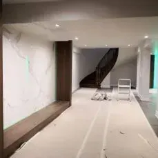 Basement renovation with a curved staircase, marble accent wall, and wood column.