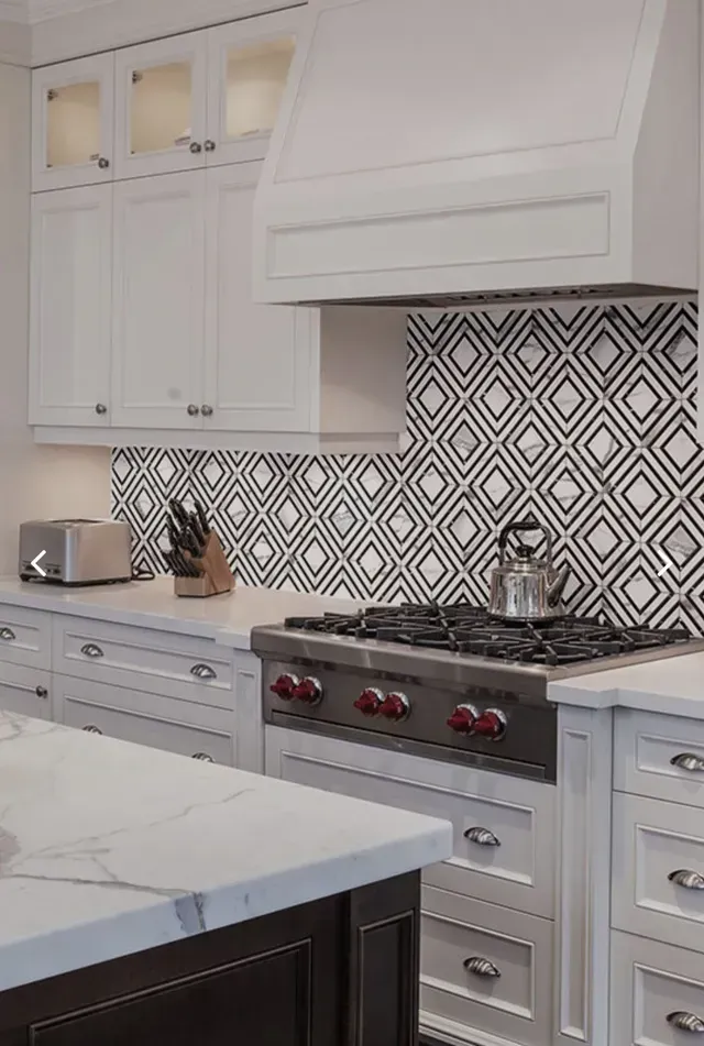White kitchen with patterned backsplash, stainless steel stove, and marble countertops.