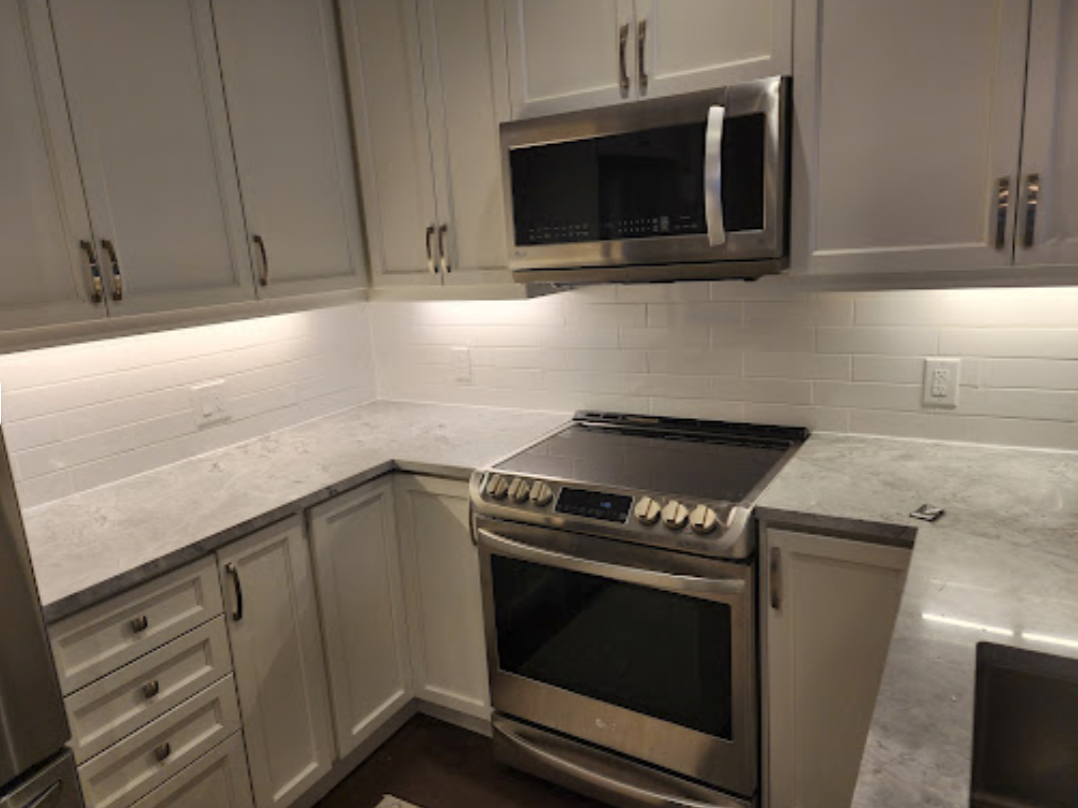 A kitchen with white cabinets , a stove , a microwave , and a sink.