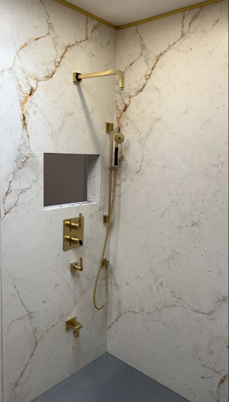 A shower with a marble wall and a gold shower head.