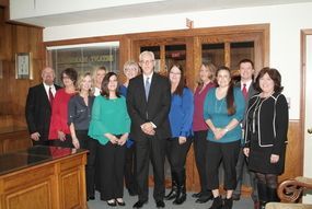 Group of people posing indoors in a wood-paneled office, dressed in business attire.