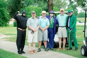 Six golfers posing on a path beside a golf cart at a course, smiling and waving