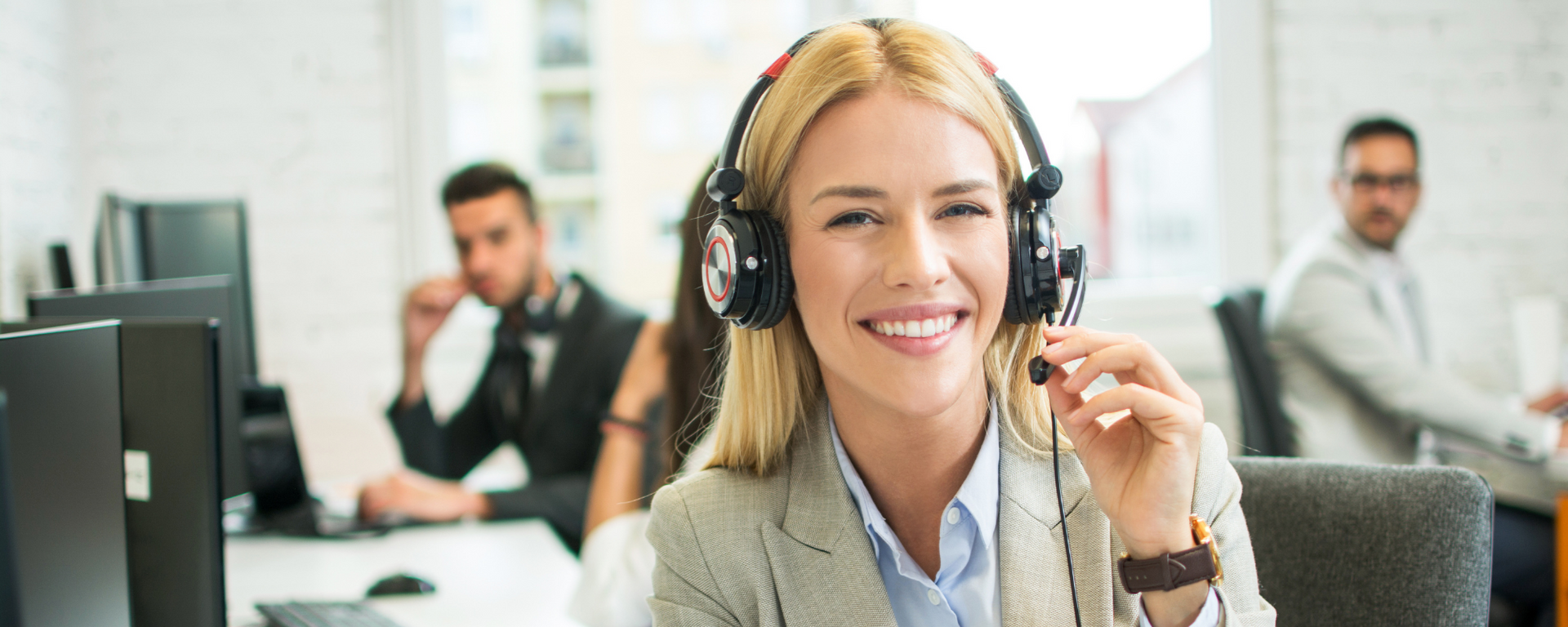 Smiling headset-wearing customer service agent at a computer in a busy office