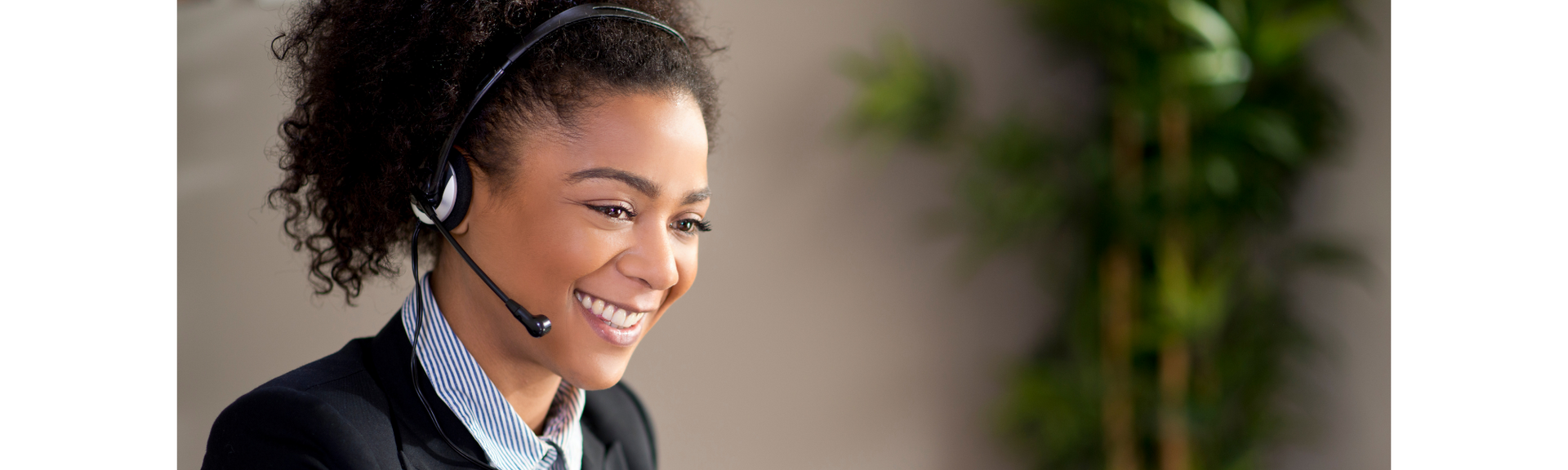 Smiling headset-wearing customer service agent at a computer in a busy office