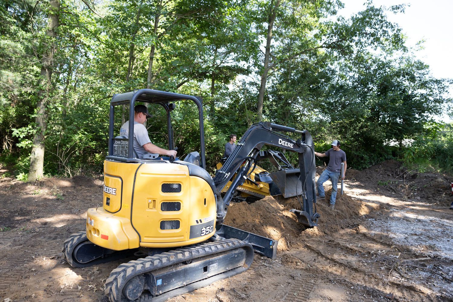 A man is driving a small excavator in a muddy field.