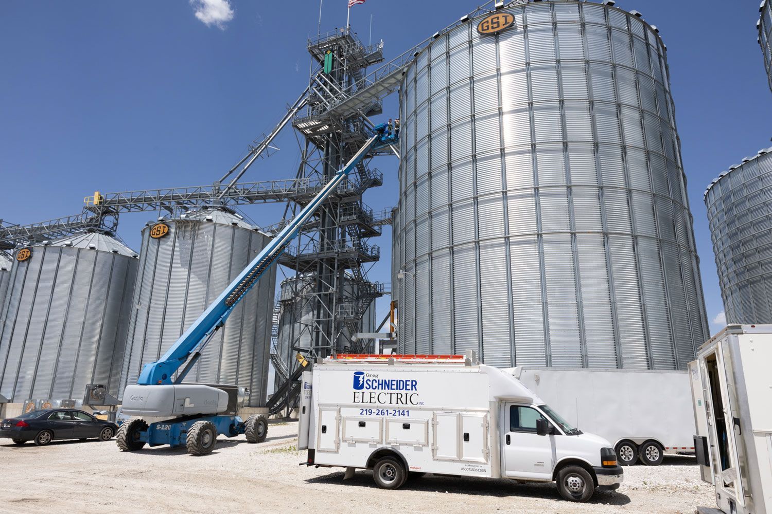 A white van is parked in front of a large silo.