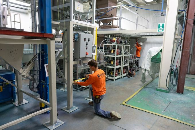 A man in an orange shirt is working on a machine in a factory.