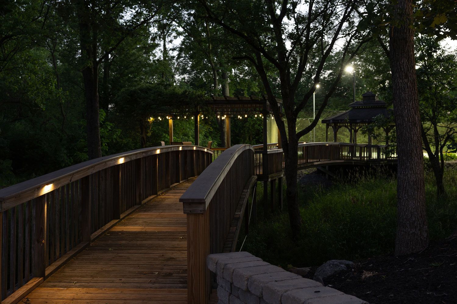 A wooden bridge is lit up at night in a park