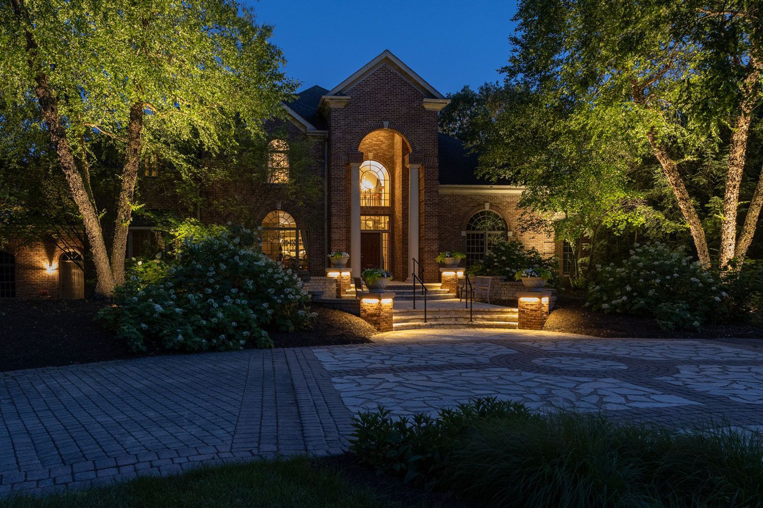 A large brick house is lit up at night with trees in front of it.