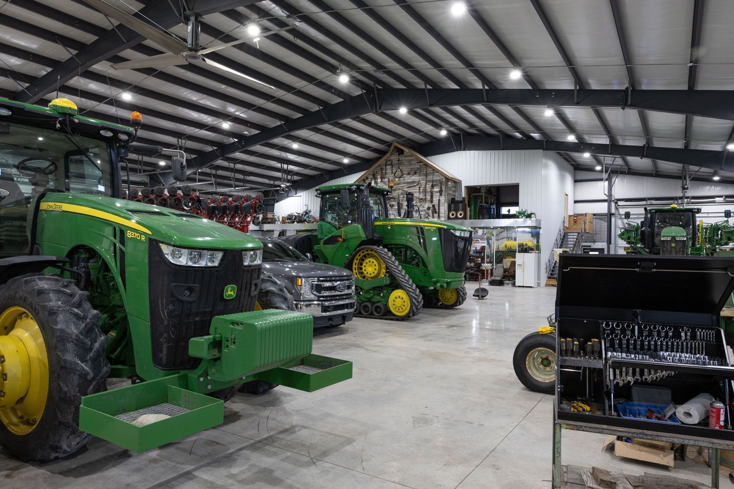 A row of green john deere tractors are parked in a warehouse.