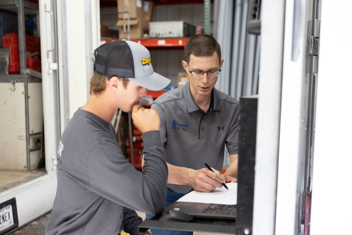 Two men are working on a computer in a warehouse.