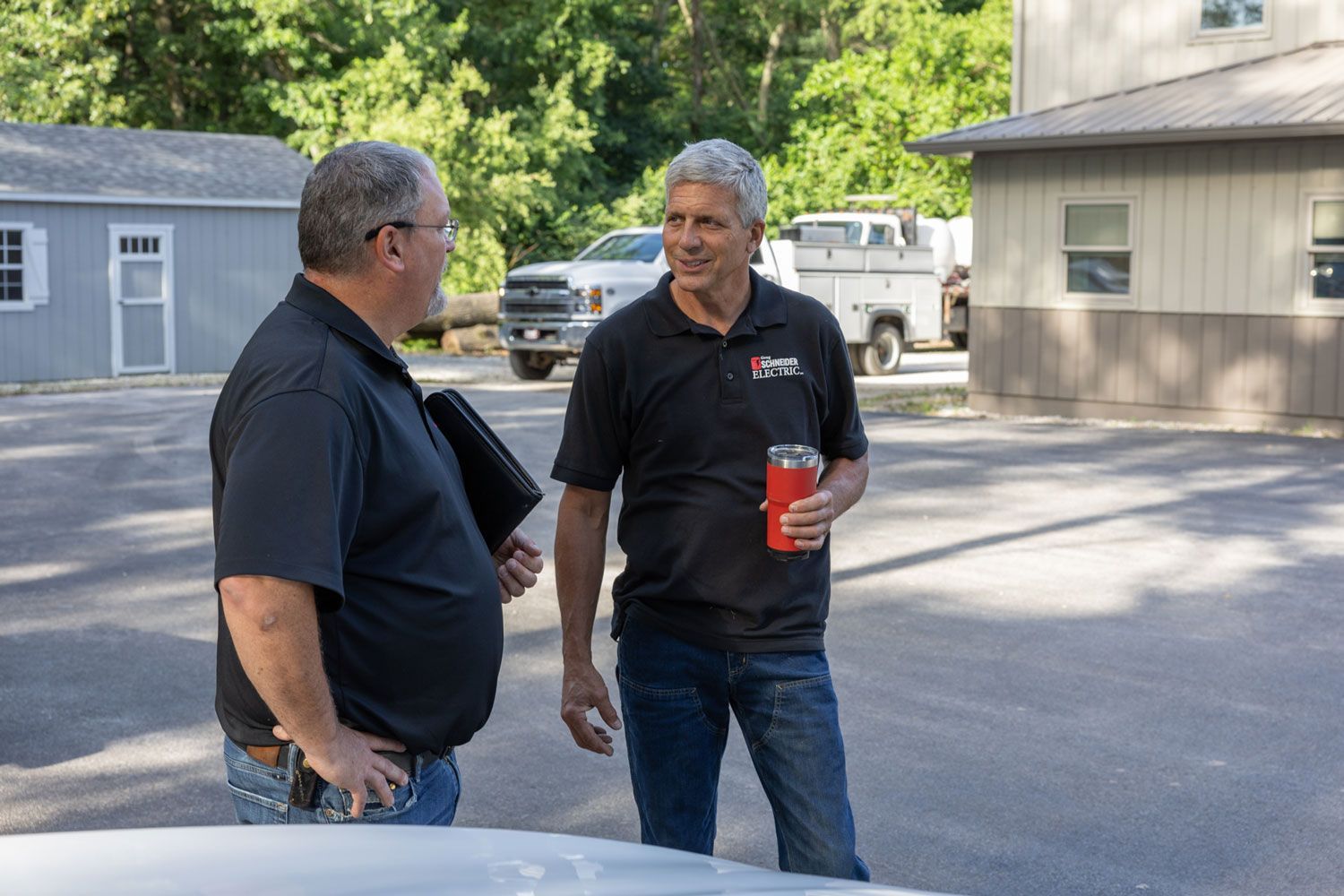 Two men are standing in a parking lot talking to each other.