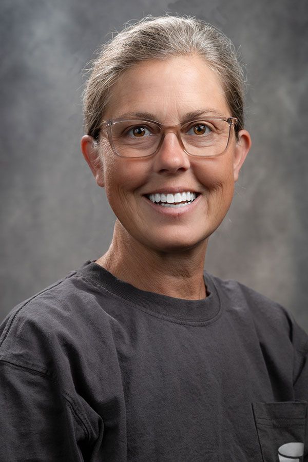 A woman wearing glasses and a gray shirt is smiling for the camera.