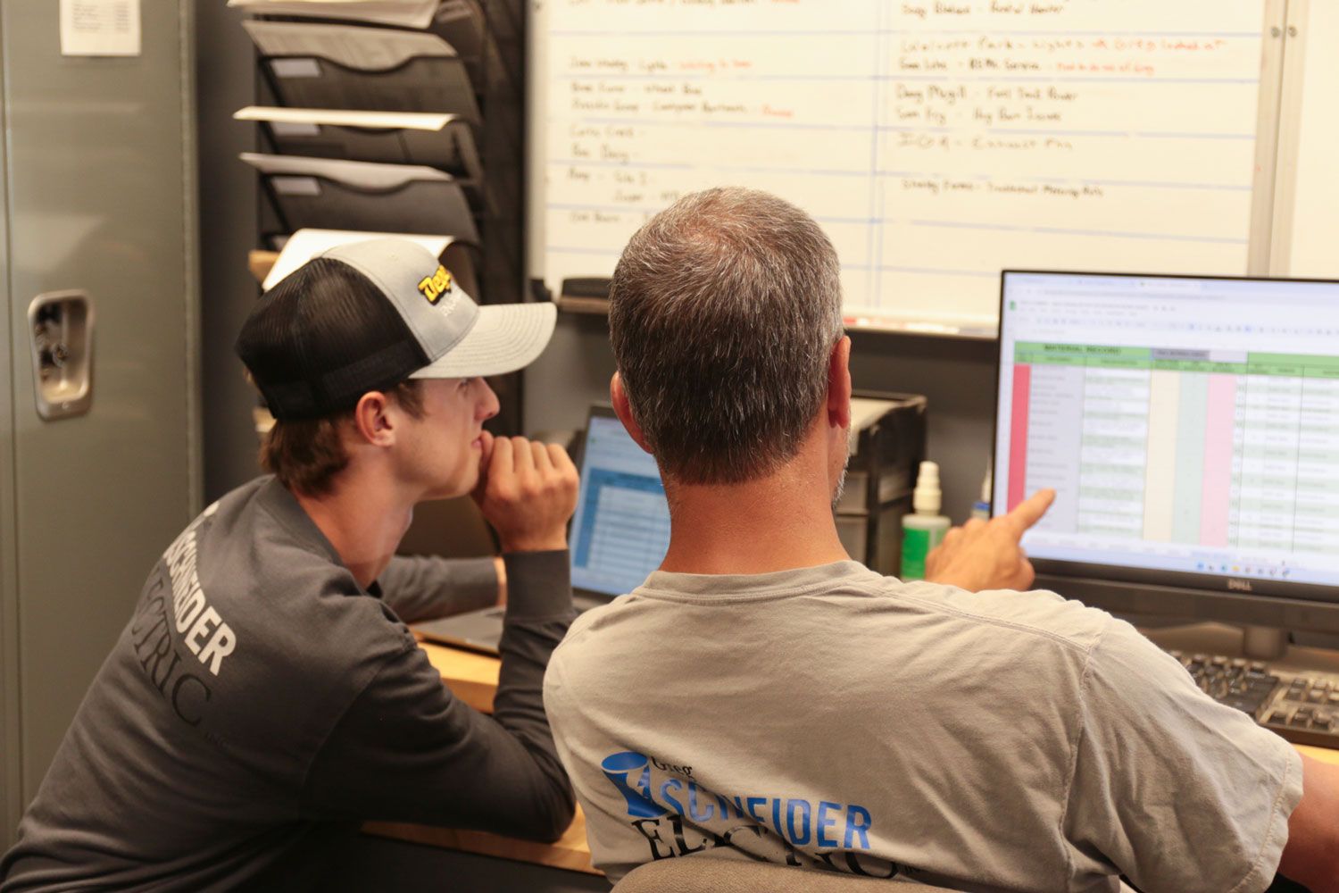 Two men are sitting at a desk looking at a computer screen.