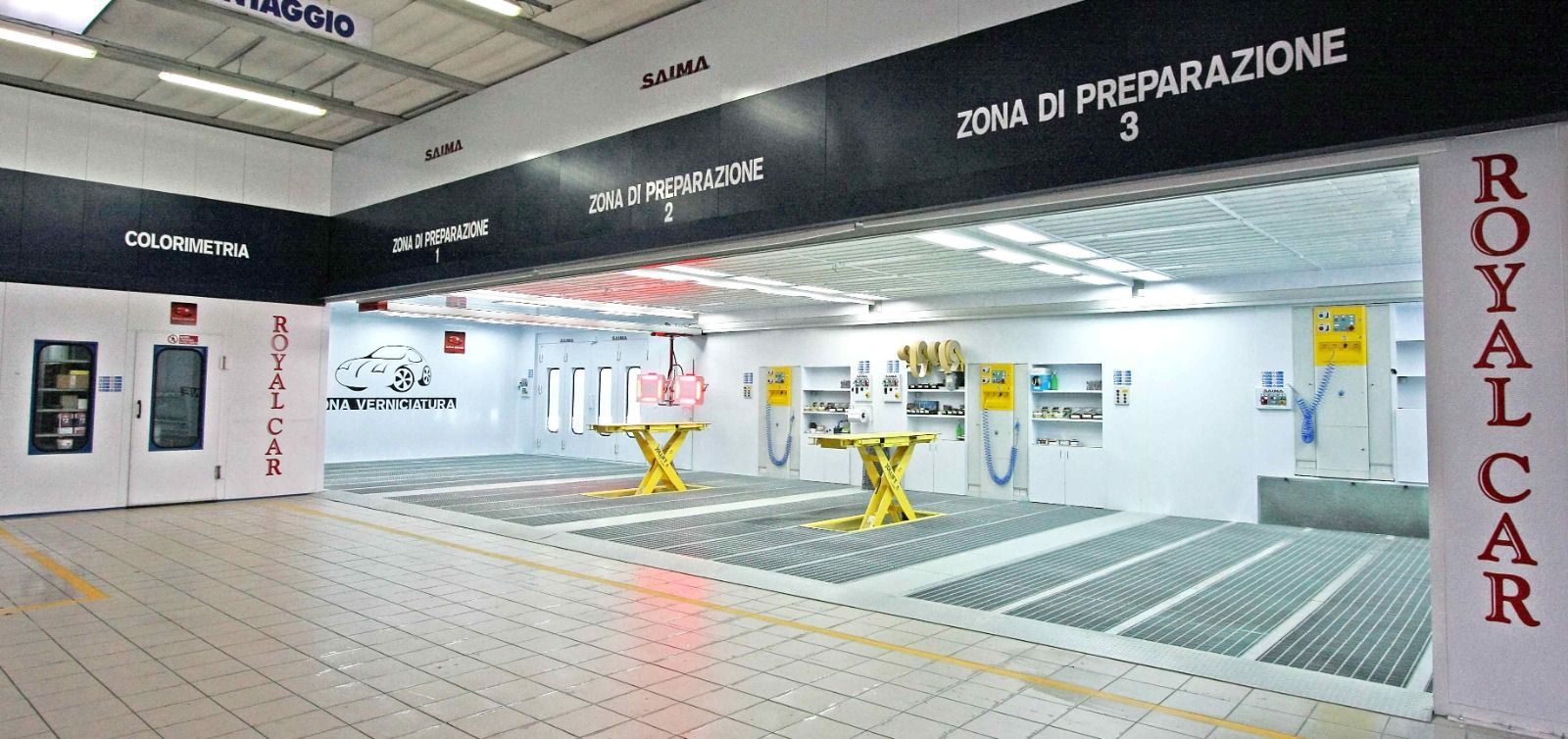 Area di servizio Royal Car Wash con macchine per la pulizia gialle e insegne italiane in un luminoso spazio interno.