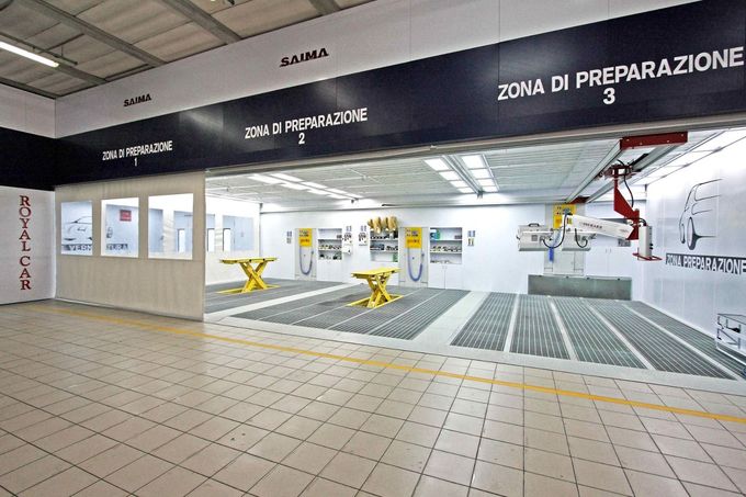 Lavanderia industriale con zone di preparazione etichettate, pavimento piastrellato e tavoli per attrezzature di colore giallo.
