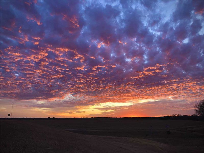 Dramatic purple and orange sunset over a dark open landscape with clouds filling the sky