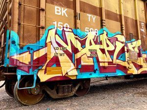 Graffiti mural on a brown freight train car with blue, pink, and yellow paint accents.