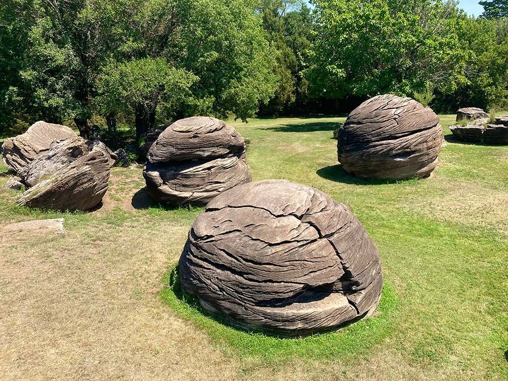 Large rounded rock formations on a grassy lawn with trees in the background, Rock City, Minneapolis, Kansas
