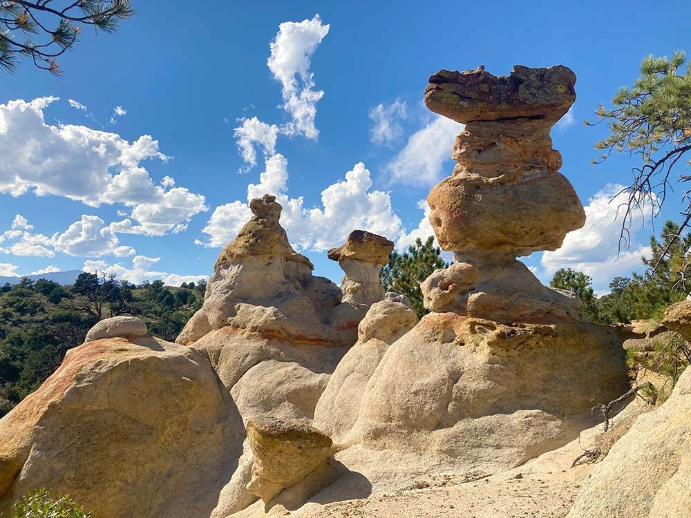 Weathered sandstone hoodoos under a bright blue sky with scattered clouds in a rocky desert landscape, Palmer Park, Colorado Springs, Colorado
