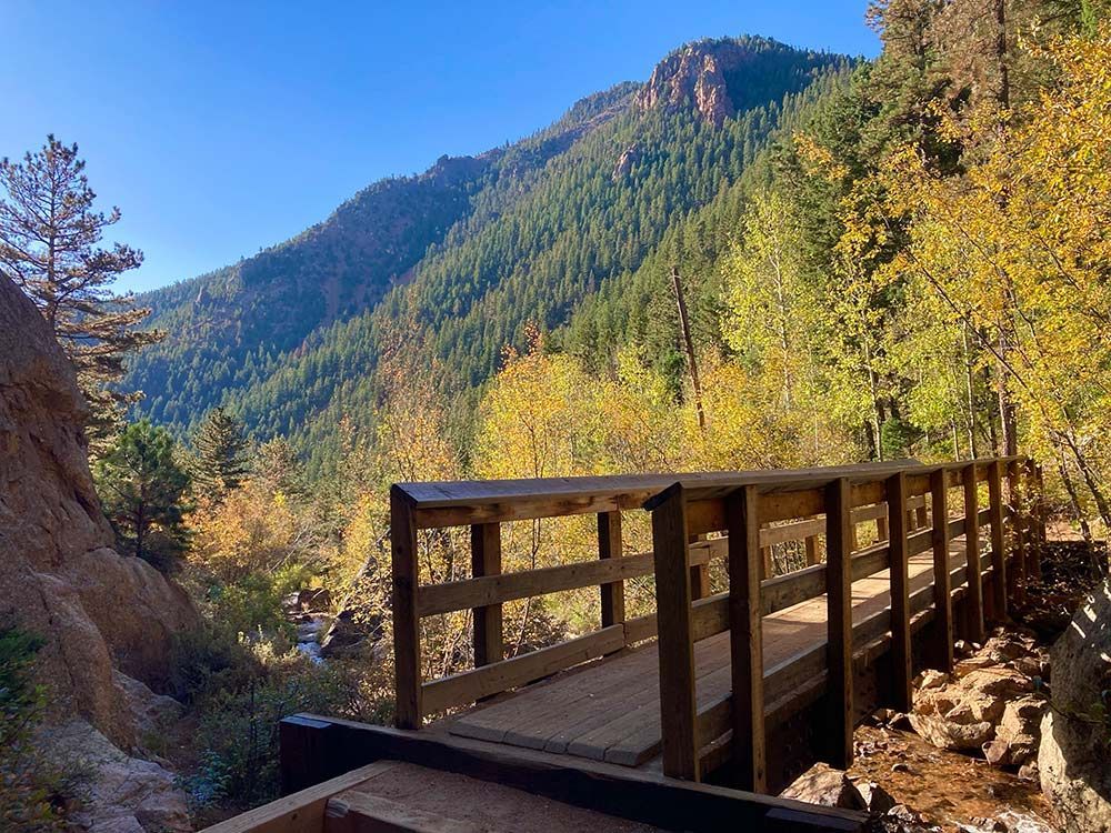 Wooden bridge on a mountain trail with autumn trees and sunlit forested hills, Seven Bridges Trail, Colorado Springs, Colorado 