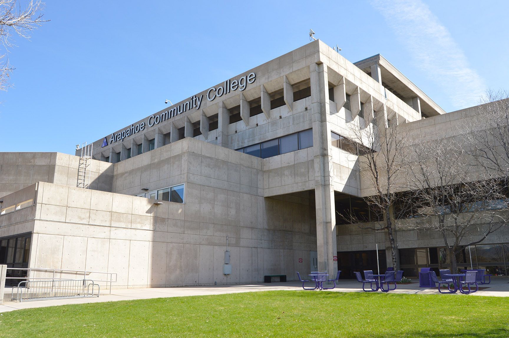 Modern concrete building with large overhang, blue sky, and green lawn in front