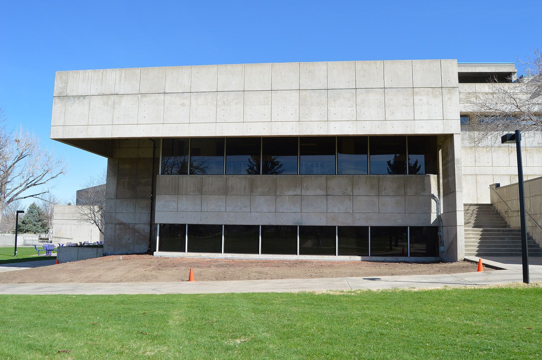 Modern concrete building with dark windows, stone side wall, and green lawn in front