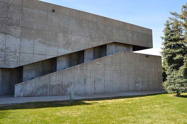 Modern concrete building with angular overhangs beside a grassy lawn and trees