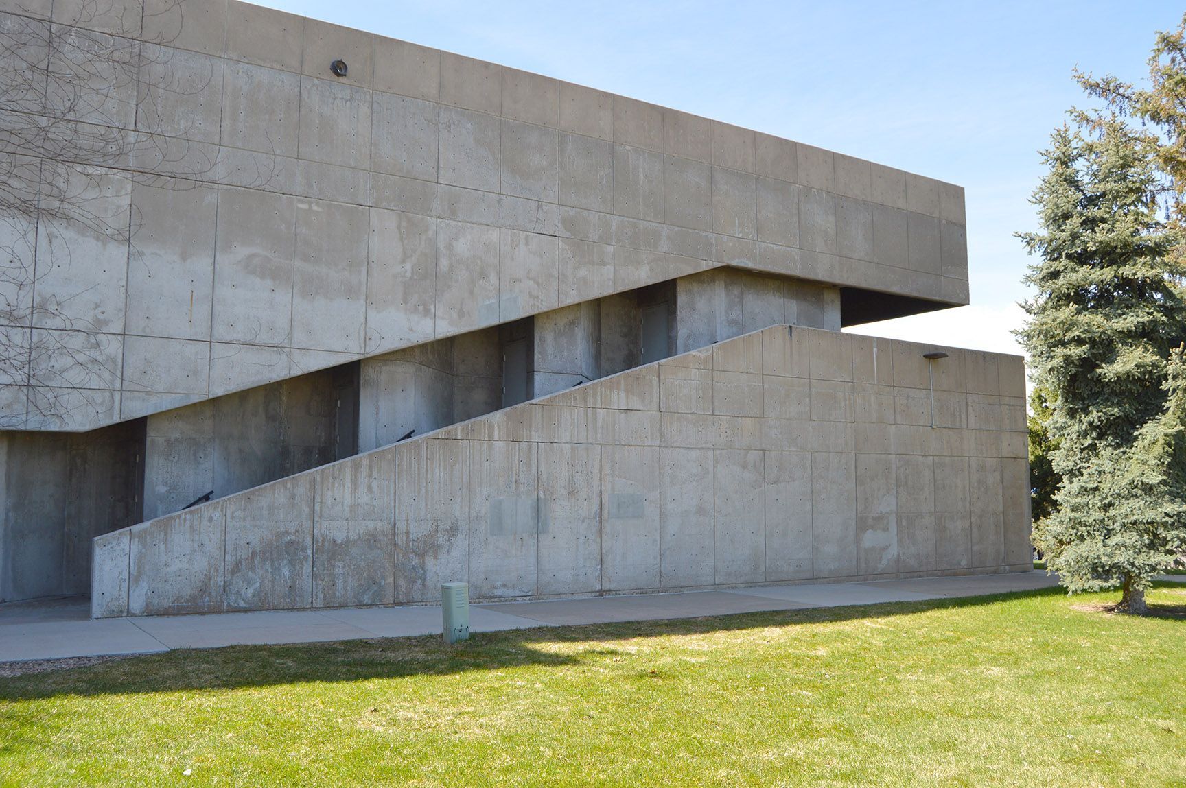 Modern concrete building with angular walls beside a grassy lawn and trees