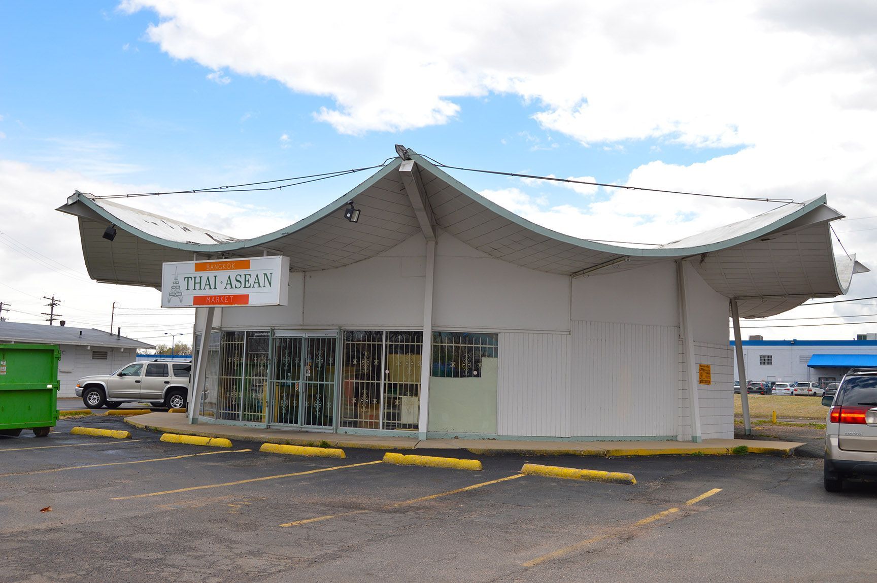 White roadside tent shop with a curved roof and open front, parked cars beside it on a gravel lot.