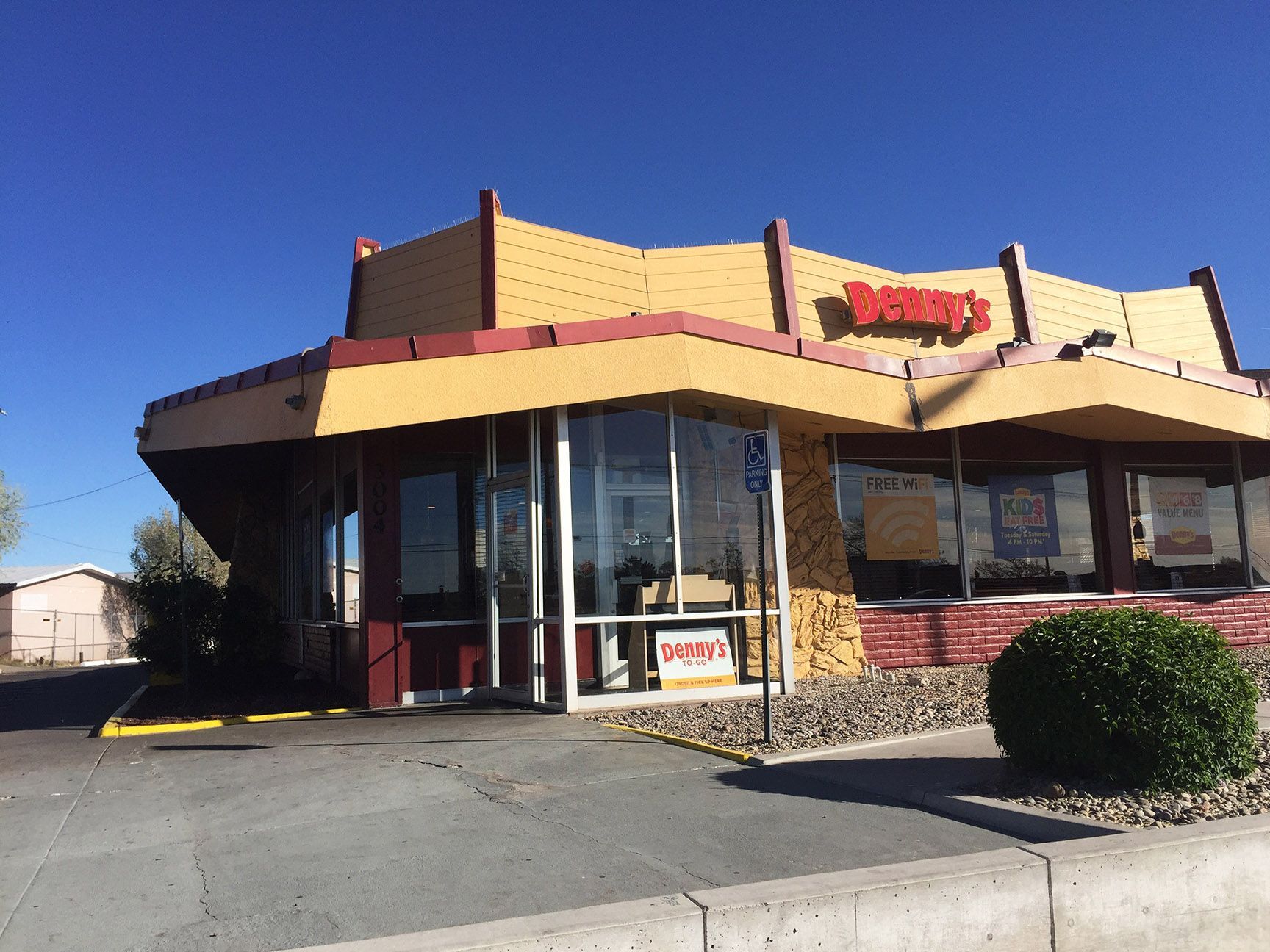 A tan fast-food restaurant with red trim and a drive-thru window on a sunny day.