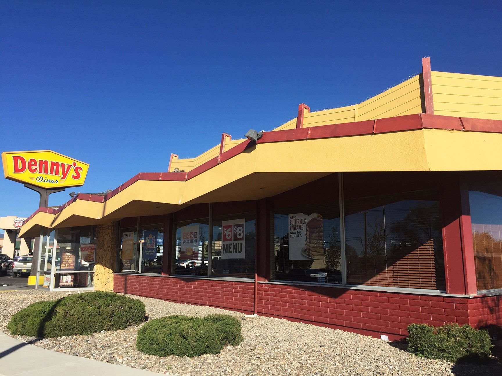 Denny’s restaurant exterior with a yellow sign, red trim, and desert landscaping under a clear blue sky