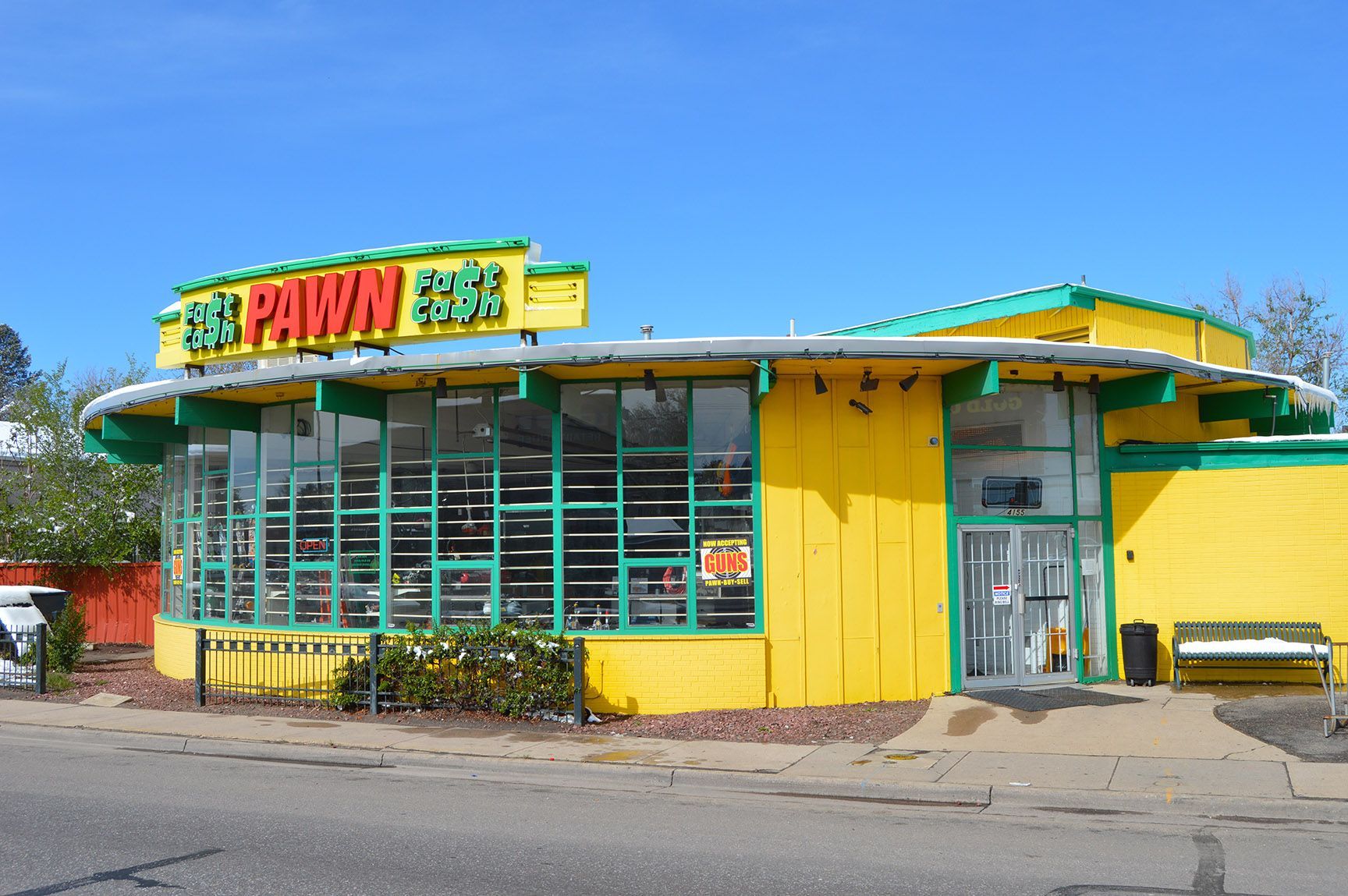 Bright yellow pawn shop with green trim and large front windows on a sunny street corner.