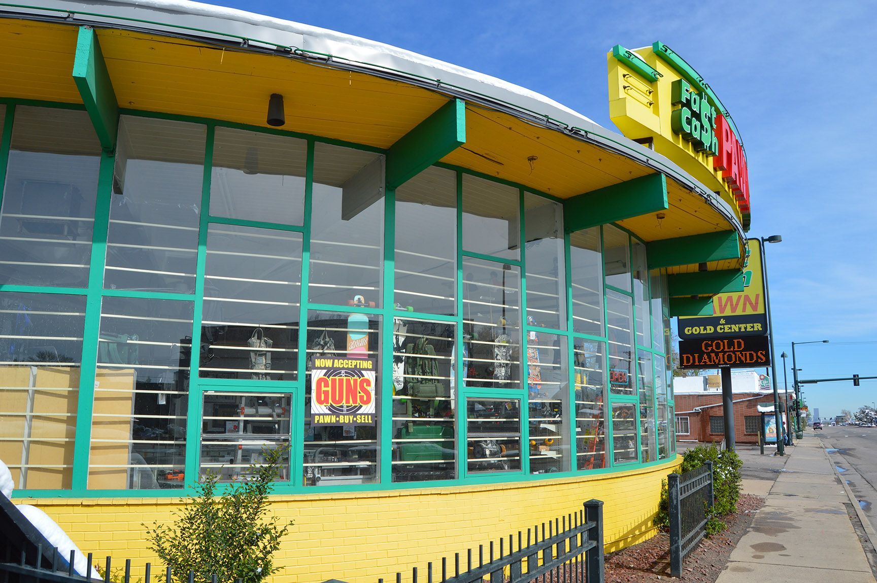 Colorful storefront with large glass windows and a sidewalk outside on a sunny day