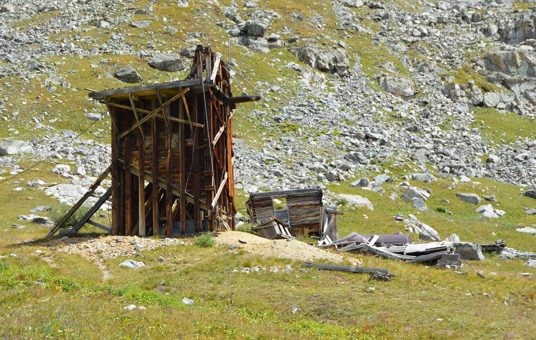 Rusty wooden shed on a grassy rocky hillside with scattered stones and debris, Mayflower Gulch, Colorado, Gold Crest Mine