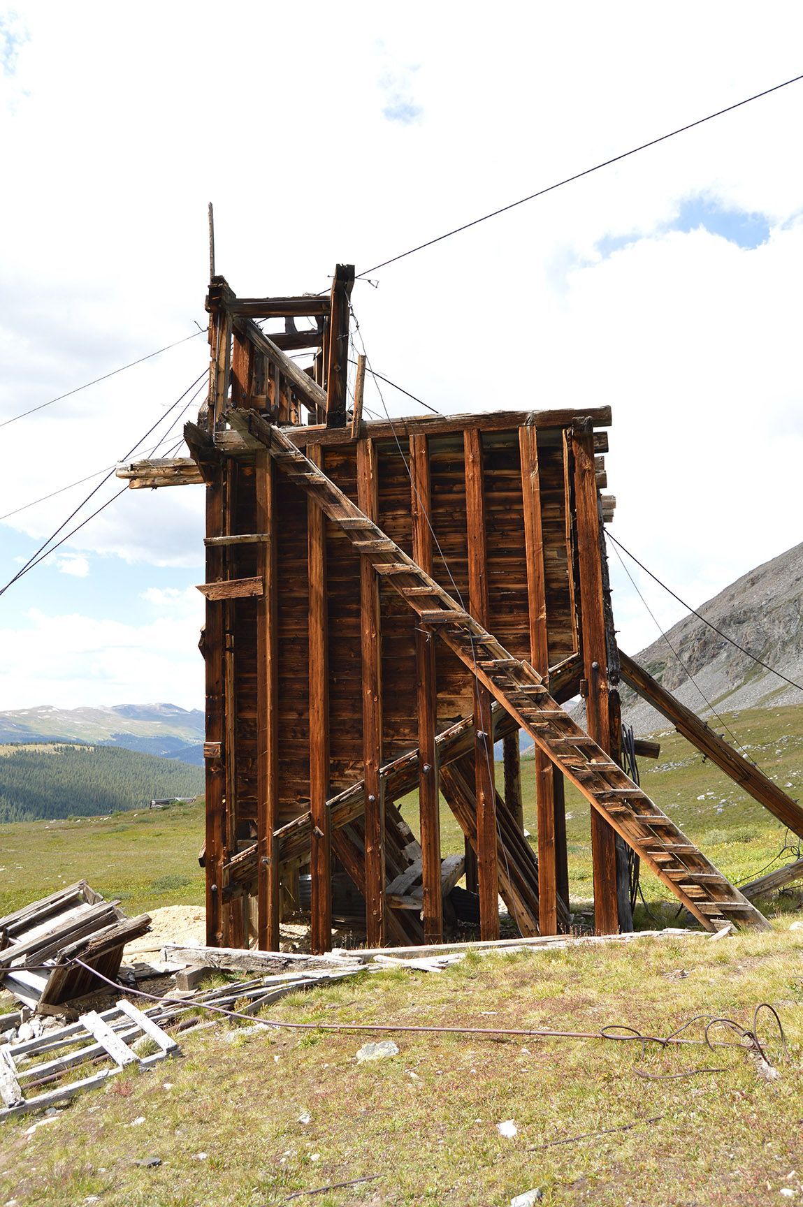 Damaged wooden mining structure on a hillside, with charred beams and a grassy landscape behind it, Mayflower Gulch, Colorado