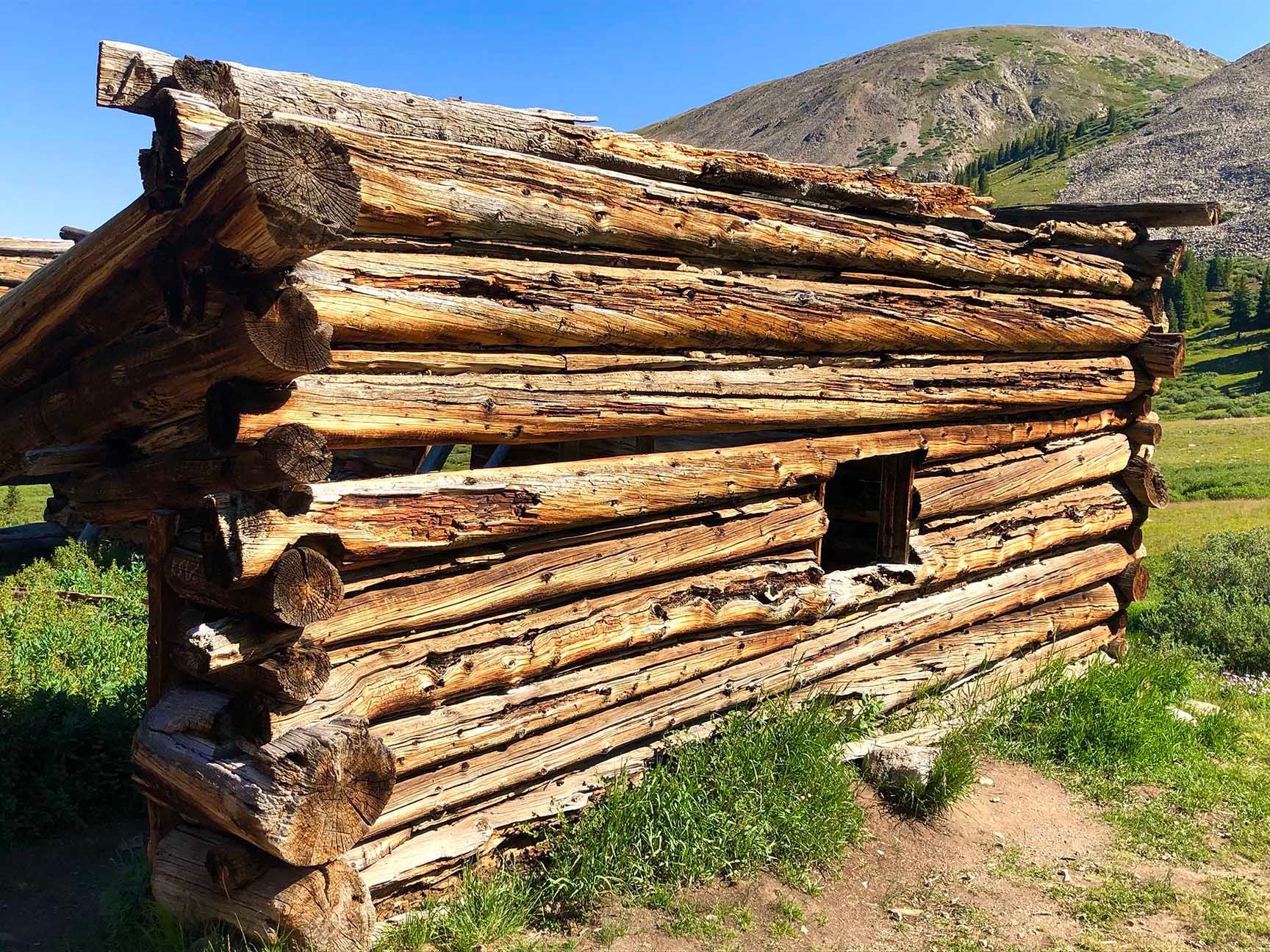 Rustic log cabin made of stacked logs in a grassy mountain setting under a clear blue sky, Mayflower Gulch, Colorado