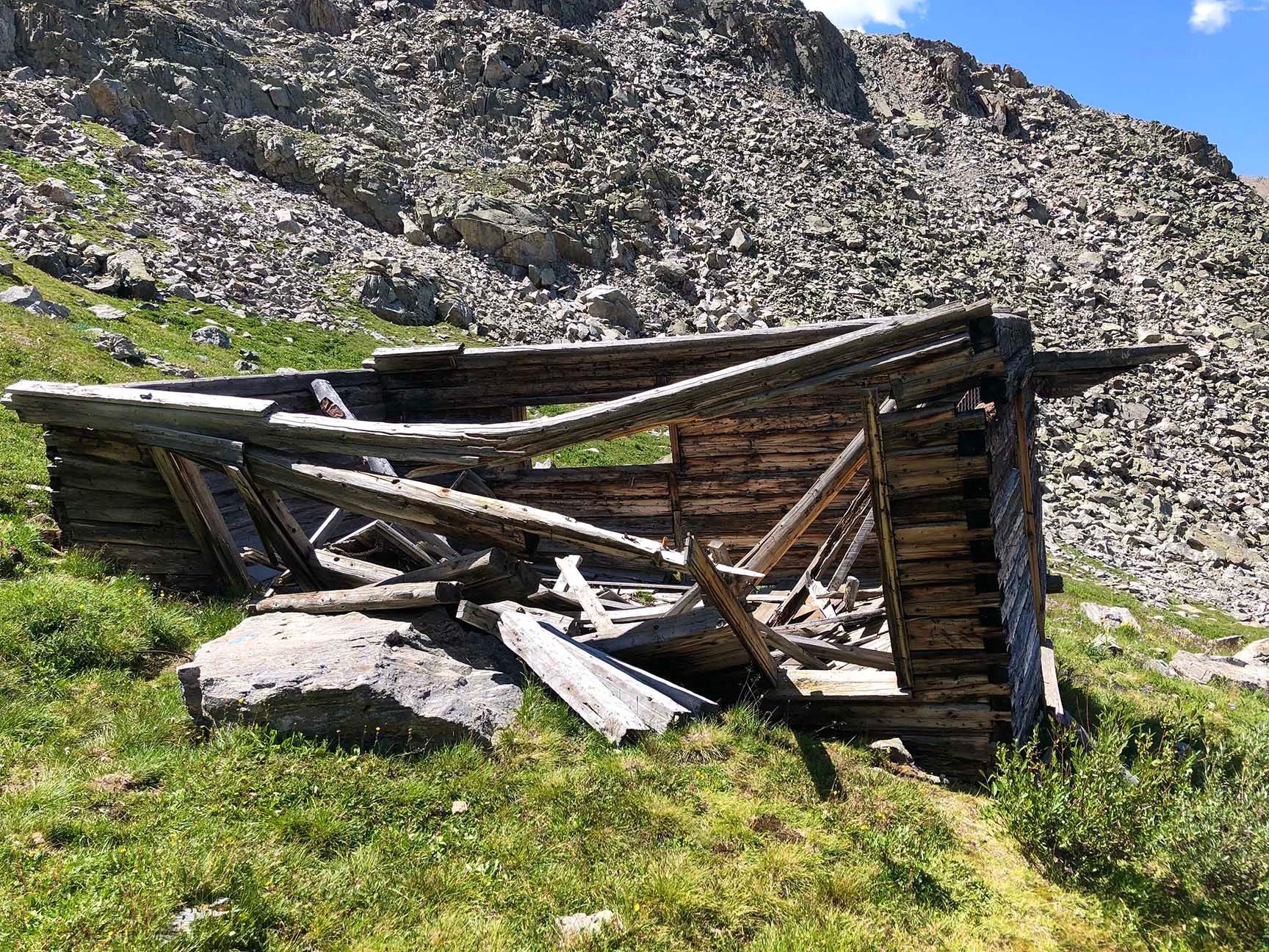 Collapsed wooden shed on a grassy mountainside beneath a rocky slope. The ruins of an old cabin, Mayflower Gulch, Colorado