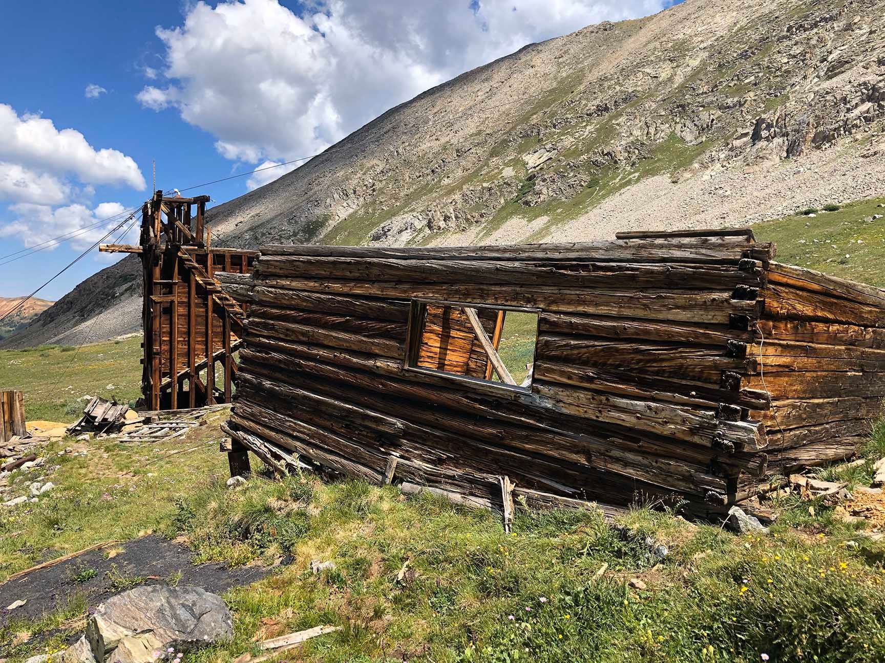 Dilapidated wooden shack in a grassy mountain landscape under a blue sky with clouds, The ruins of an old cabin, Mayflower Gulch, Colorado