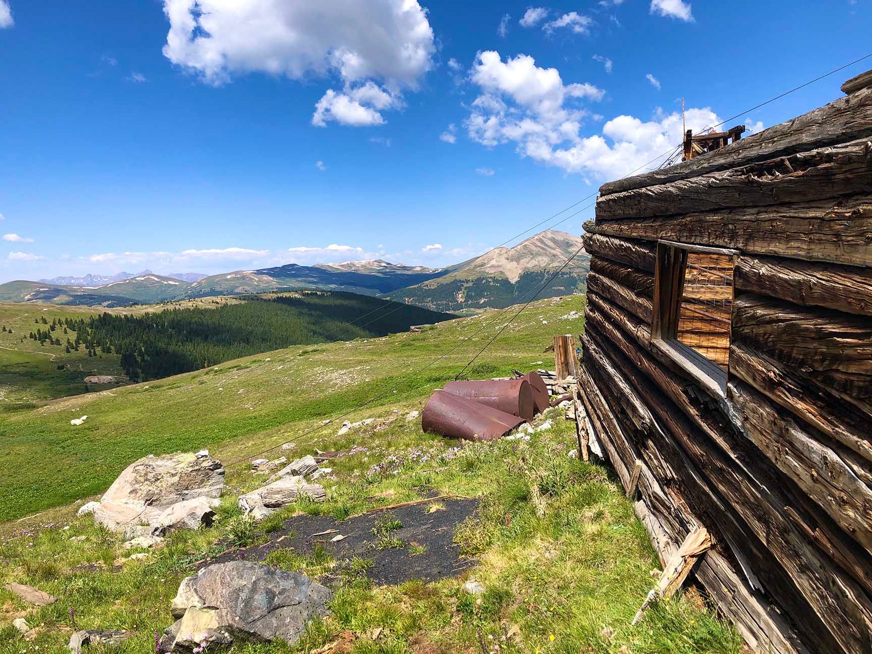 Mountain valley view from a grassy hillside beside a wooden cabin under a blue sky, The ruins of an old cabin, Mayflower Gulch, Colorado