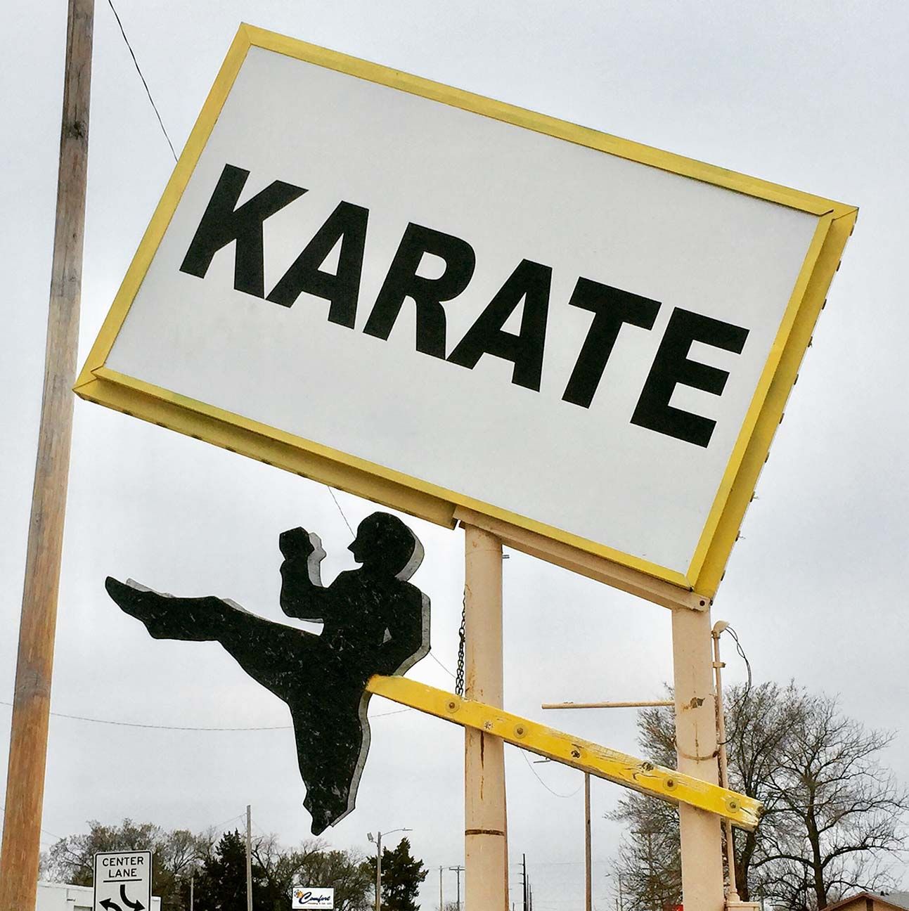 Karate sign with a black kicking silhouette on a tilted white-and-yellow board outdoors