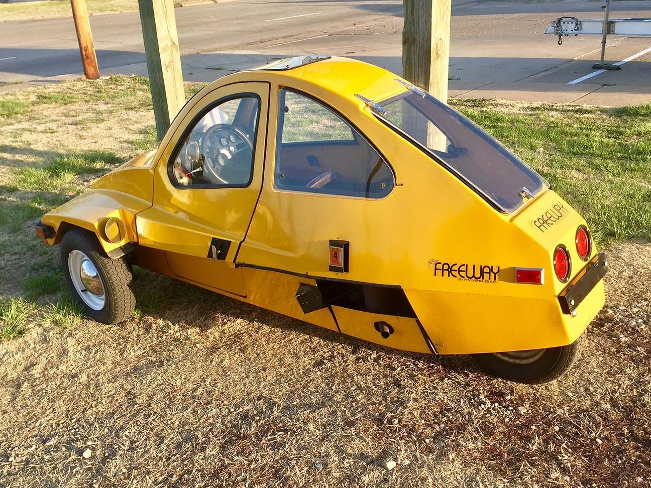 Yellow three-wheeled microcar parked on gravel near a beach path, Salina, Kansas