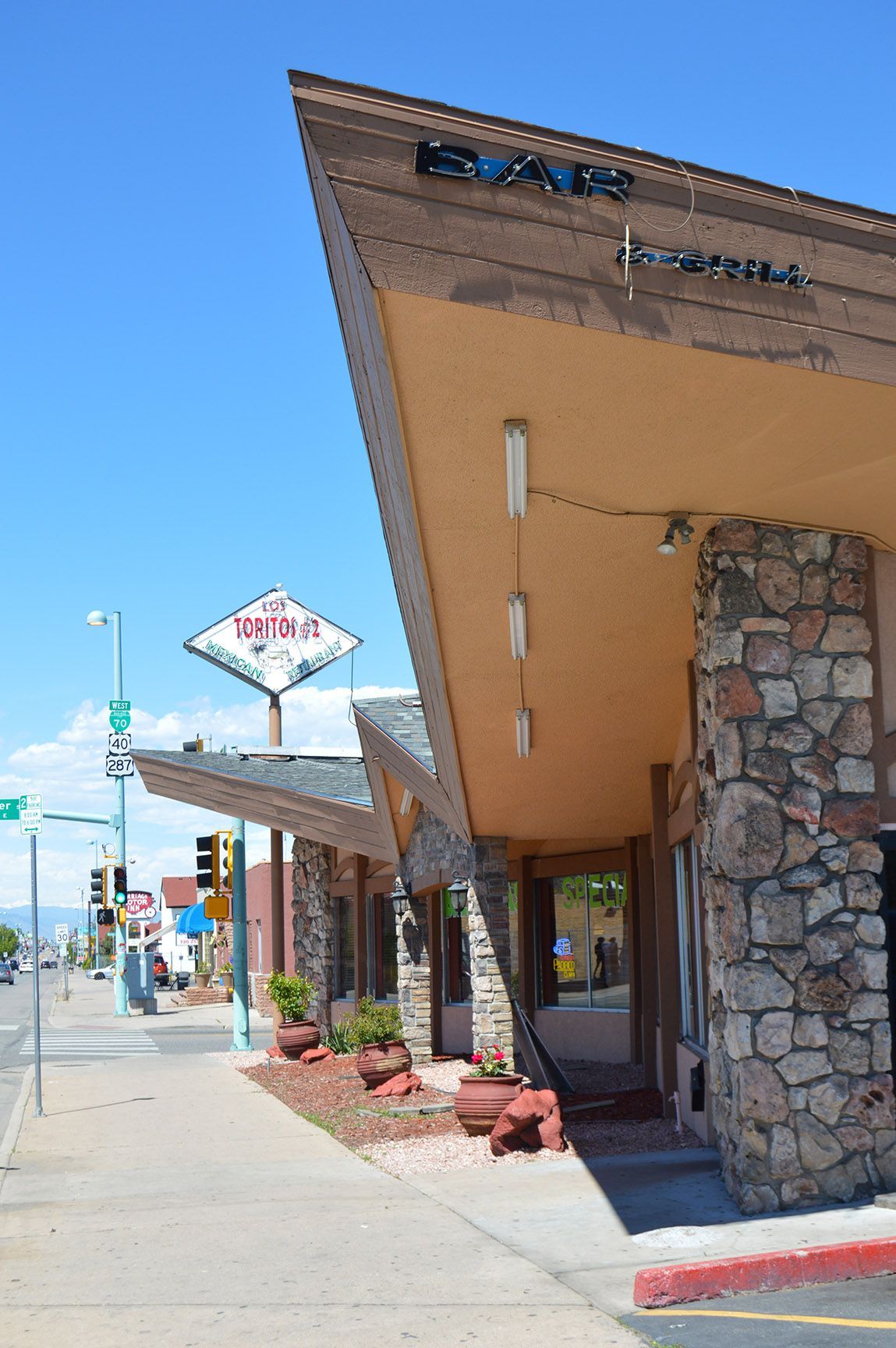 Street view of a tan stucco storefront with stone trim and a red curb under a blue sky