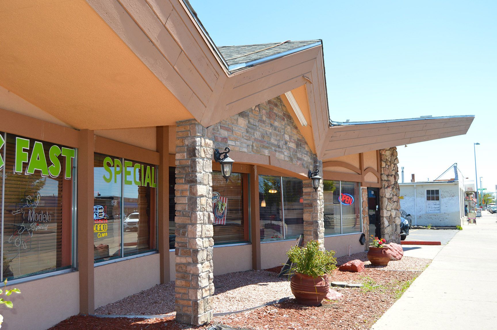 Strip mall storefronts with stone columns and a tan awning on a sunny day.
