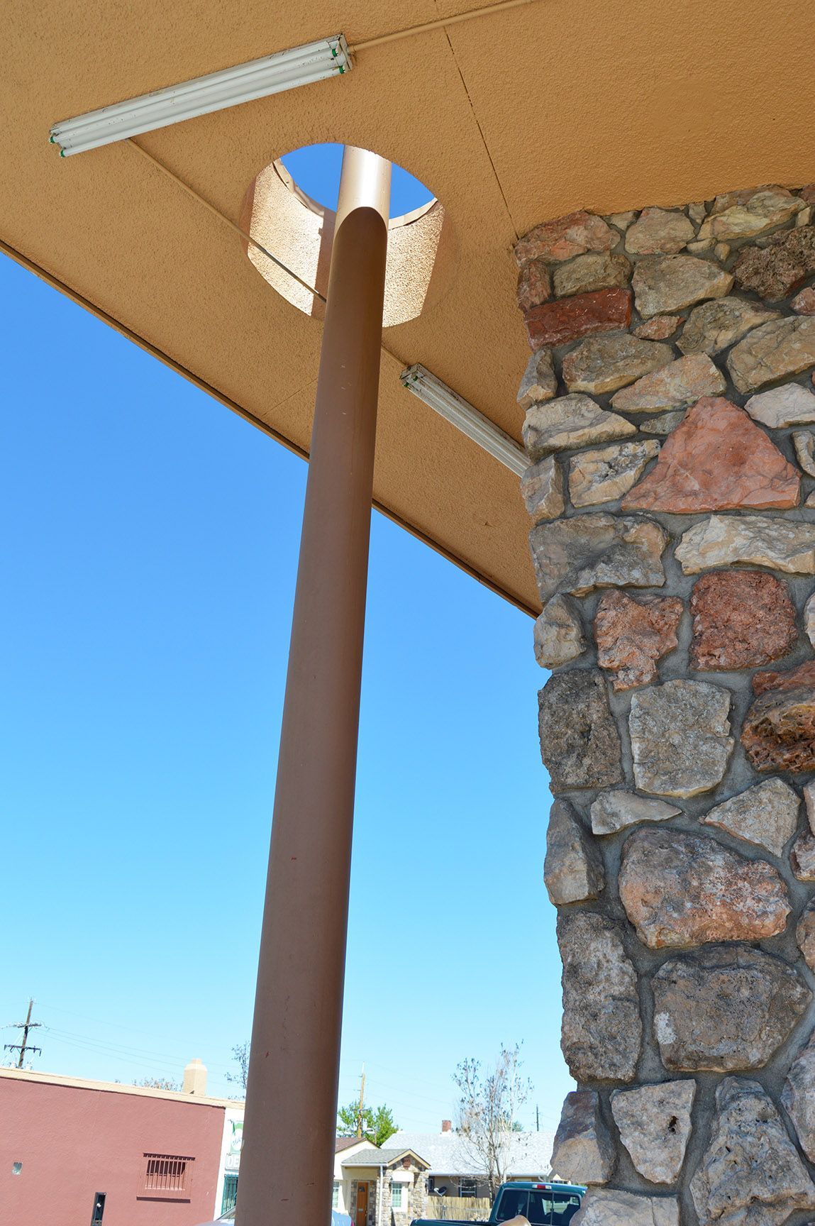 Outdoor view of a covered patio with a stone pillar and a brown support pole against a blue sky