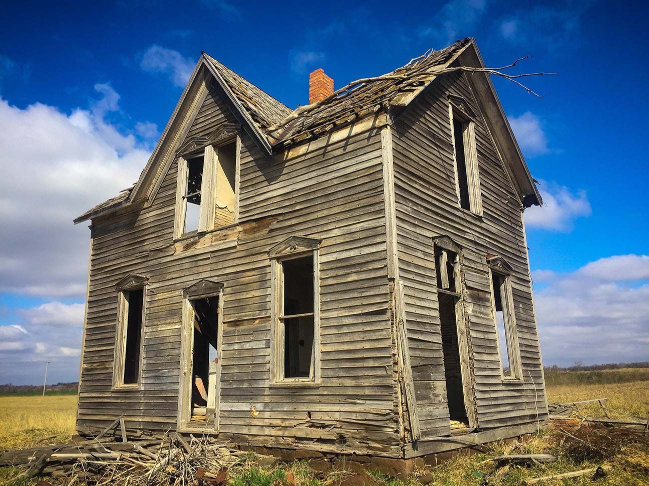 Abandoned weathered wooden house in a grassy field under a blue sky with clouds
