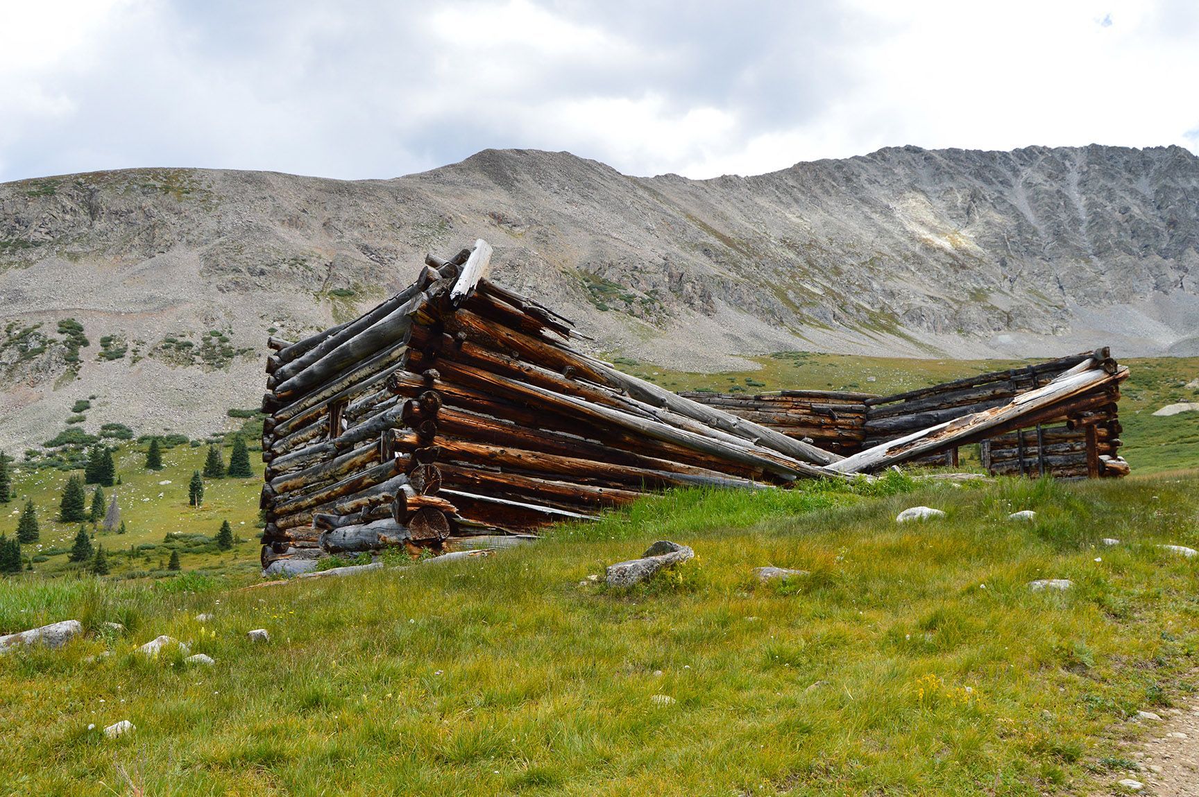 Collapsed log cabin in a grassy mountain meadow with rocky hills in the background. The ruins of an old cabin, Mayflower Gulch, Colorado